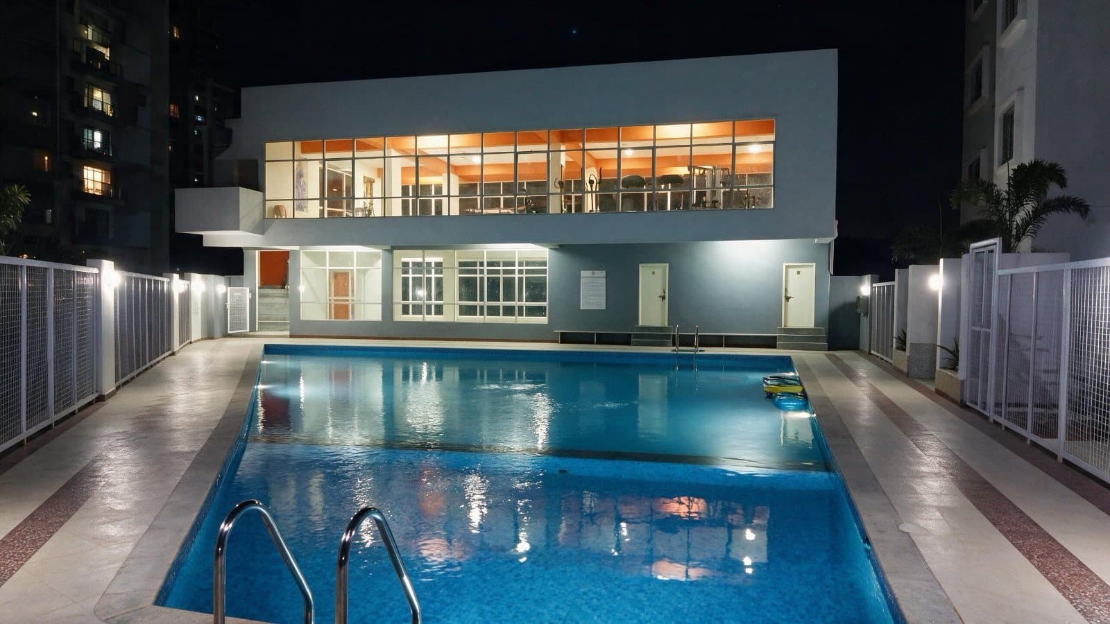 The pool lit at night, with the gymnasium glowing above the pool deck