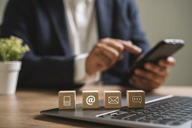 Four wooden blocks on a laptop marked with a phone, an @ sign, an envelope and a chat bubble, a person using a mobile phone behind them