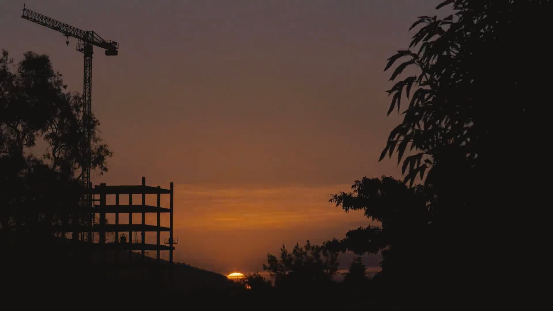 The sun rising behind a tower crane and the frame of a building under construction