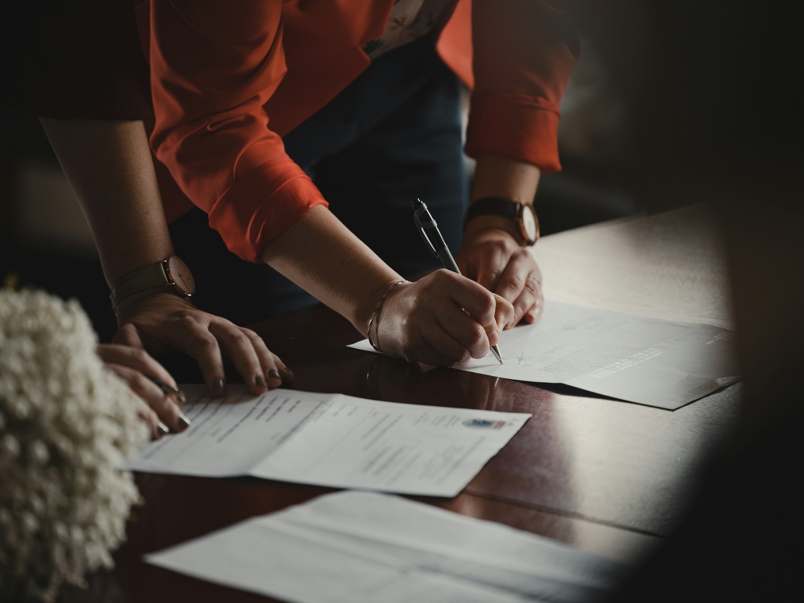 Two people either side of a desk, one signing an agreement while the other holds the papers steady