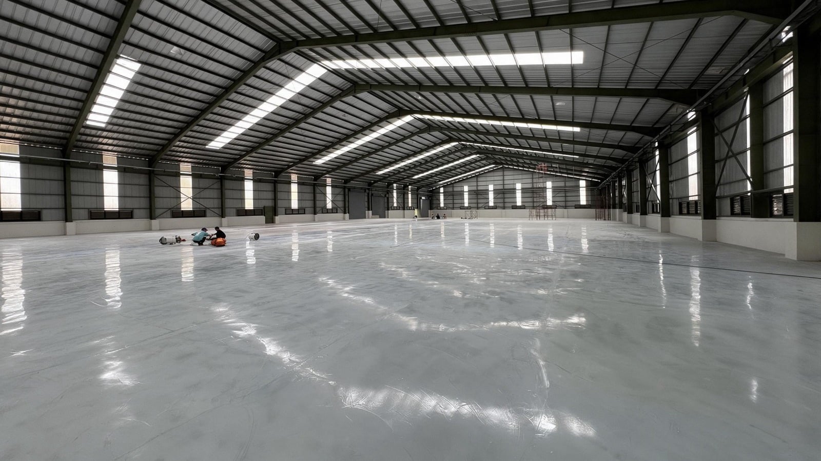 The inside of a completed pre-engineered industrial shed, its steel frame and roof lights overhead and a finished, sealed floor running the length of it